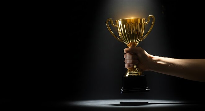 Hand holding a golden trophy cup on a dark background celebrating achievement and success conceptual image for awards ceremonies and sports competitions