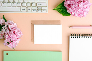 Home office desktop with computer keyboard, notepad, envelope with blank card, pen and hydrangea...