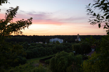 Beautiful sunset sky and tree, branch, bush on silhouette on colorful clouds from the high hill down on forest, park, architecture building. Nature in the evening time at summer. Natural real colors