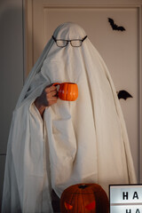 Person in costume of ghost hold pumpkin shaped cup.Halloween Vertical Spooky shot
