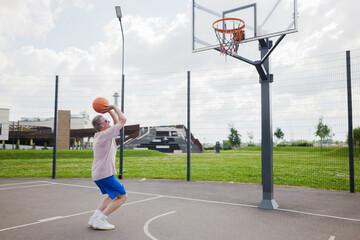 Elderly man shoots basketball in park under sunny sky