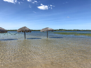 Relaxing scene at Lagoa do Paraíso in Jericoacoara, Ceará, Brazil, featuring straw huts and hammocks suspended above the clear, shallow waters of the lagoon