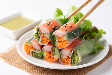 Salad roll with crab stick, carrot, cucumber and lettuce wrapped with rice paper on dish eating with dipping sauce