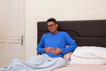 Adult Asian man on bed suffering stomach ache
