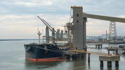 Large cargo ship is docked at an industrial port facility. Cranes loadunload goods in this busy...