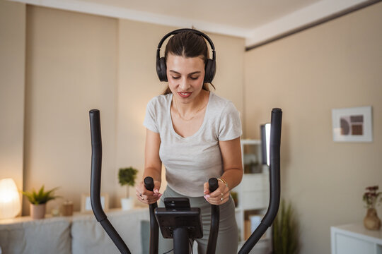 pretty woman listen music and exercise on elliptical machine at home