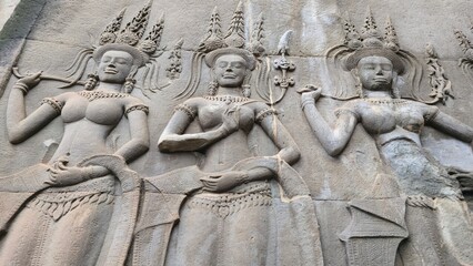 Angkor Wat, Cambodia - 3 July 2025. Stone carvings of three crowned women in ornate dress with raised arms and calm expressions line a weathered temple surface.