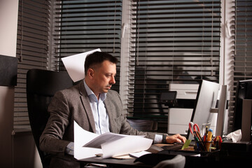 Stressed office worker typing on laptop as papers fly around him. Overwhelmed business atmosphere,...