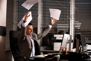 Frustrated businessman throws documents in the air, expressing stress and burnout. Office...