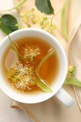 Fresh linden tea in cup and flowers on white table, flat lay