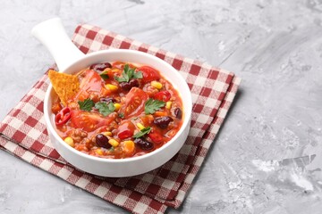 Tasty chili con carne in bowl and nachos on grey textured table, closeup. Space for text