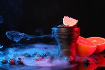 Hookah bowl with smoke and fruits on black table in neon lights, closeup