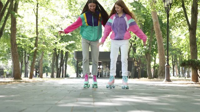 Two teenage girls roller skating together on city street, low angle view