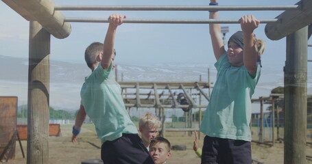 Swinging children hanging from metal monkey bars at playground obstacle course, with worn tires