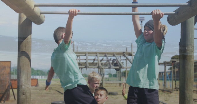 Swinging children hanging from metal monkey bars at playground obstacle course, with worn tires