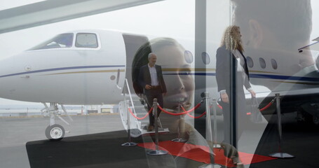 Descending businessman wearing dark suit stepping onto red carpet on airport ramp, with private jet
