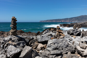 Balanced stone towers on rocky coastal cliffs overlooking the Atlantic Ocean under a clear blue sky in Portugal.