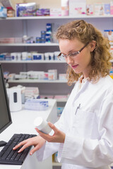 Female pharmacy technician entering data at counter holding medicine bottle typing on keyboard