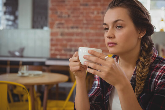 Woman holding ceramic mug and gazing right at cafe wooden table with yellow chairs, copy space