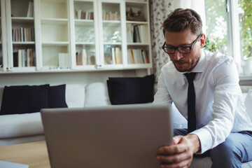 Middle-aged man in business attire adjusting laptop on table in living room, copy space