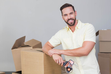 Man leaning on cardboard box while sealing boxes with tape dispenser in new room