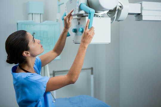 Female radiologic tech in scrubs adjusting Xray handles checking panel in imaging suite, copy space - Powered by Adobe