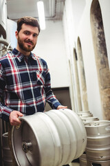 Beer keg resting waist-high in brewery storage corridor, with stacked kegs and fermentation tank