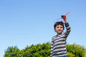 Boy holding red toy airplane overhead in backyard under clear blue sky, copy space