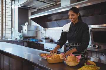 Indian chef in chef coat arranging bread and pastry baskets on table in kitchen, copy space