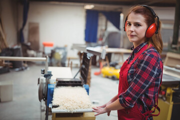 Female carpenter with red apron and earmuffs using planer in workshop making shavings, copy space