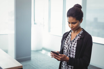Asian and African American woman standing by window in office holding smartphone, copy space