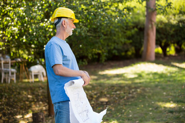 yellow hard hat resting beside blueprints on grassy lawn in filtered sunlight with white chairs