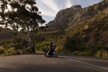 Female skateboarder crouching low on longboard under white helmet gliding down mountain road