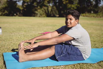 Asian child stretching forward on blue yoga mat in park with pink mat and water bottle