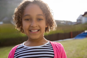 Child girl standing in grassy yard wearing striped shirt and pink cardigan under bright sky