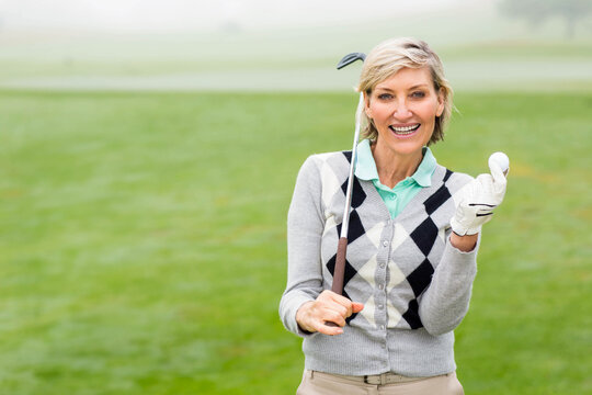 Senior female golfer holding club on shoulder and displaying ball with glove on fairway, copy space