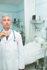 Male physician holding syringe and stethoscope at hospital room with bed and IV pole, copy space
