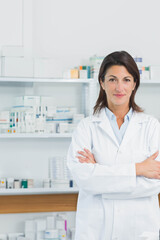 Female pharmacist in white lab coat standing arms crossed in pharmacy by pill bottles, copy space