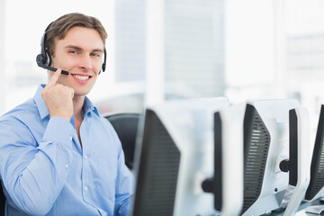 Man wearing business shirt pointing at headset microphone sitting at desk with monitors, copy space
