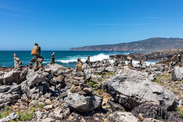 Balanced stone towers on rocky coastal cliffs overlooking the Atlantic Ocean under a clear blue sky in Portugal.