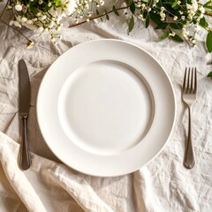 Elegant Table Setting with White Plate, Cutlery, and Delicate Floral Arrangement, Top View.