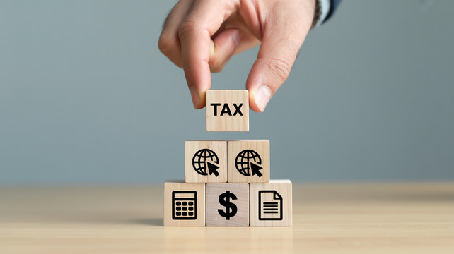 Hand Placing Wooden Block on Pyramid of Light Beige Cubes on Wooden Surface