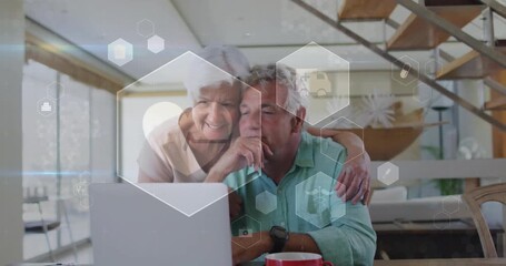 Senior woman embracing senior man opening laptop animating hex tech icons and reviewing options - Powered by Adobe