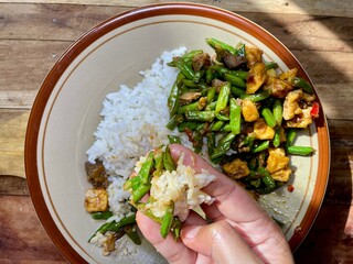 a woman's hand is eating rice, a side dish of stir-fried long beans isolated on ceramic plate on...