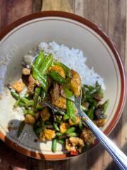 close up view, stir fry long beans on stainless spoon with white rice background and side dishes isolated on ceramic plate on table, simple healthy home cooking, stir fry long beans, liver and gizzard
