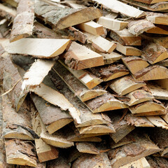 Detailed view of raw, unevenly chopped firewood with bark, showing texture and grain in a freshly cut timber pile.