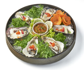 Fresh oysters served on bed of ice with vibrant garnishes, including lettuce, lemon slices, chili, and carrot flowers, accompanied by tangy dipping sauce
