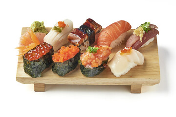 Wooden platter of assorted sushi including nigiri and gunkan featuring fresh salmon tuna shrimp scallop eel and roe garnished with wasabi and pickled ginger presented on white background