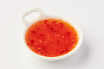 Small white bowl filled with vibrant red sweet chili sauce, showcasing mix of chili flakes and glossy texture, perfect for dipping or as condiment