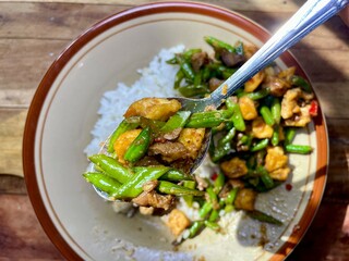close up view, stir fry long beans on stainless spoon with white rice background and side dishes isolated on ceramic plate on table, simple healthy home cooking, stir fry long beans, liver and gizzard